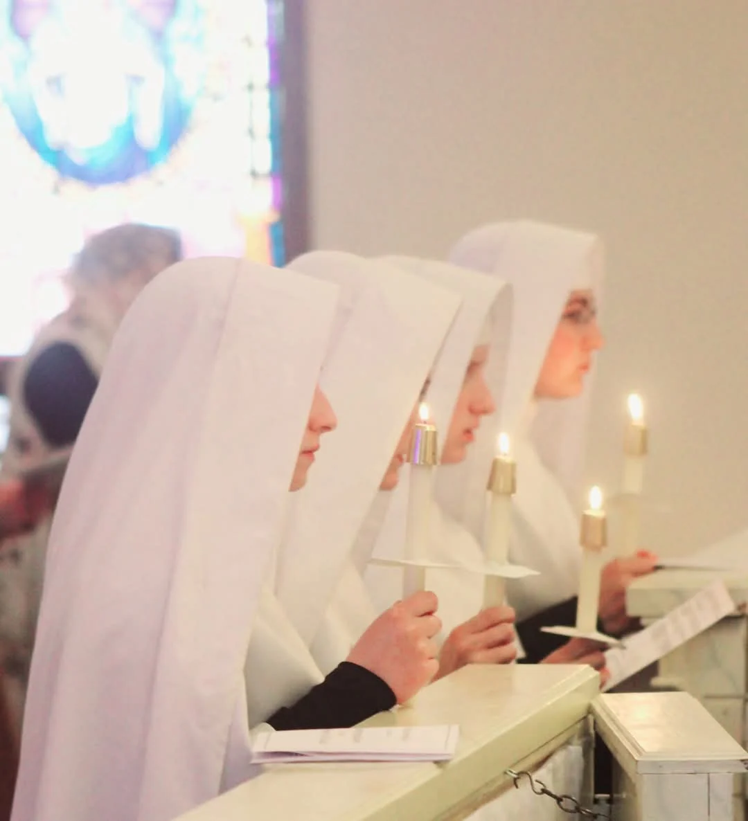 Sisters holding candles in prayer during a religious ceremony.